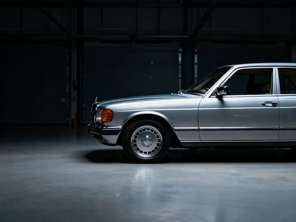 Srebrny Mercedes W126 coupe w ujęciu profilowym, zaprezentowany w klimatycznym, industrialnym garażu.
